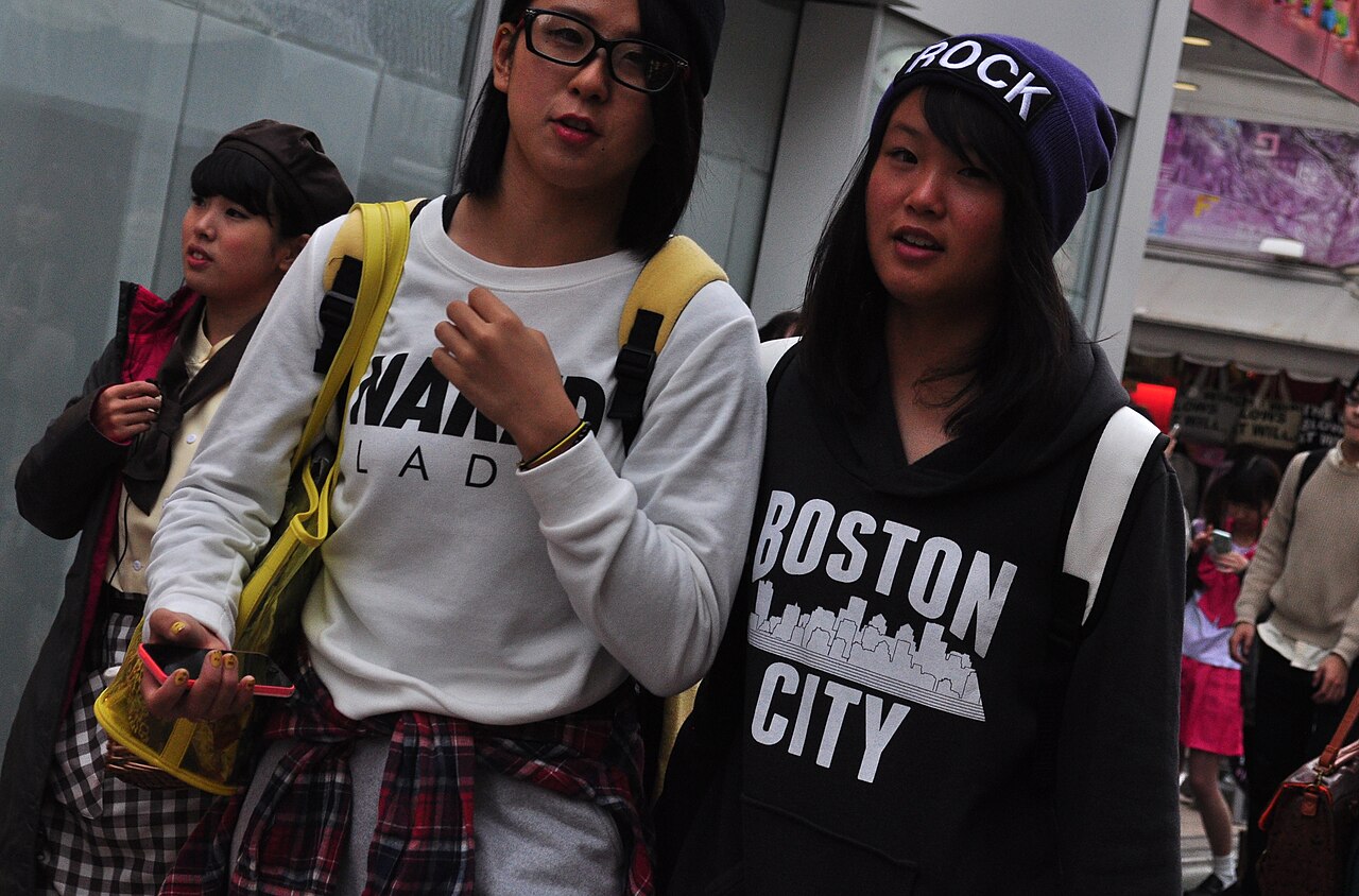 Three young people on a Harajuku street in graphic print sweatshirts, a plaid shirt tied at the waist and knit beanies