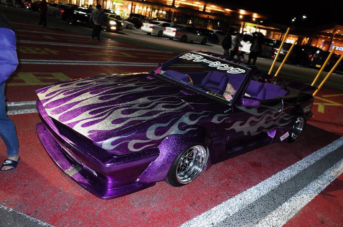 Purple bosozoku kaido racer car with silver flame paint, wide body kit and tall exhaust stacks parked at a night meet