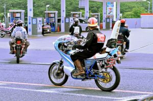 Bosozoku riders on customised motorcycles with tall rocket cowls and kanji jackets pulling out of a Japanese petrol station