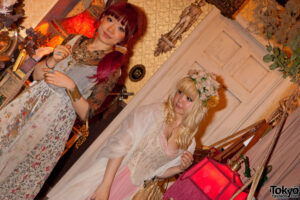 Two women in dolly kei coordinates wearing layered lace, floral prints and antique jewellery indoors