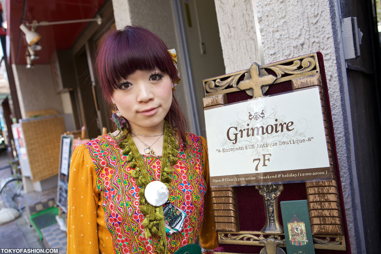 Woman in an embroidered vest and tasselled necklace beside the Grimoire European and US Antique Boutique sign