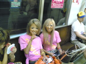 Two ganguro girls in Tokyo with deep tans, bleached blonde hair, white eye makeup and pink logo tees