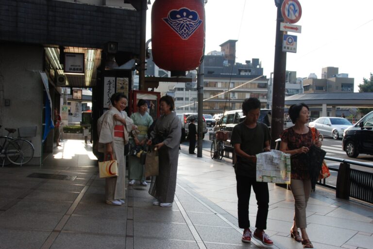 Three women wearing kimono with obi sashes tied, walking on a street in Kyoto, Japan