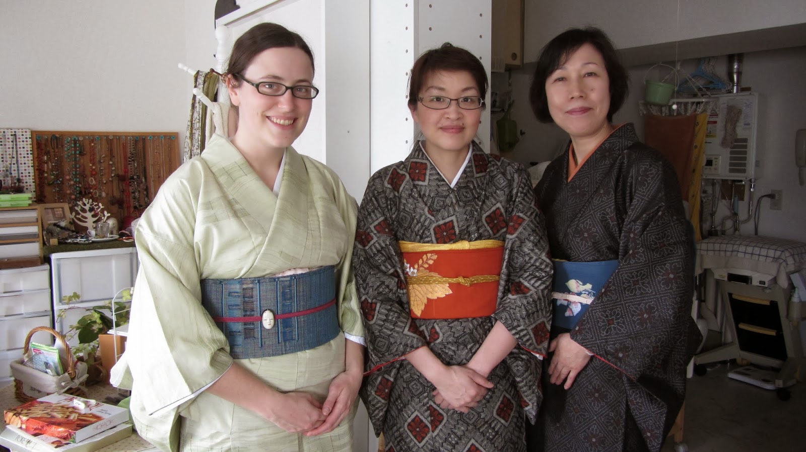 Three women wearing kimono with differently tied obi belts in blue, orange and patterned fabric