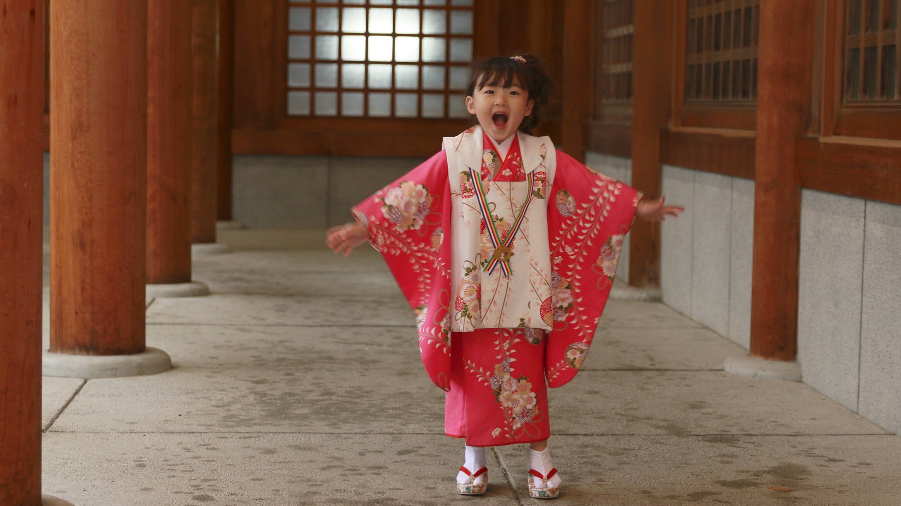 Child in a floral kimono with sleeves spread, showing the body panels and layered white collar underneath