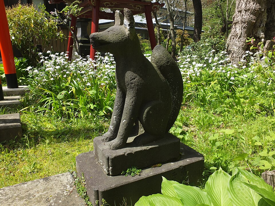 Weathered stone fox statue on a plinth beside a red torii gate at an Inari shrine