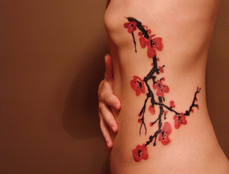 Cherry blossom branch tattoo in red and black ink running along a person's ribs and hip