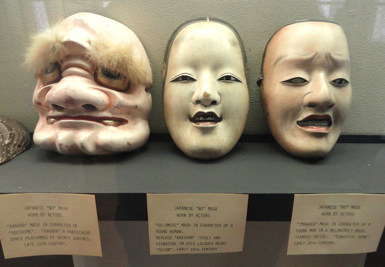 Three carved Japanese Noh and Kagura masks displayed side by side in a museum case