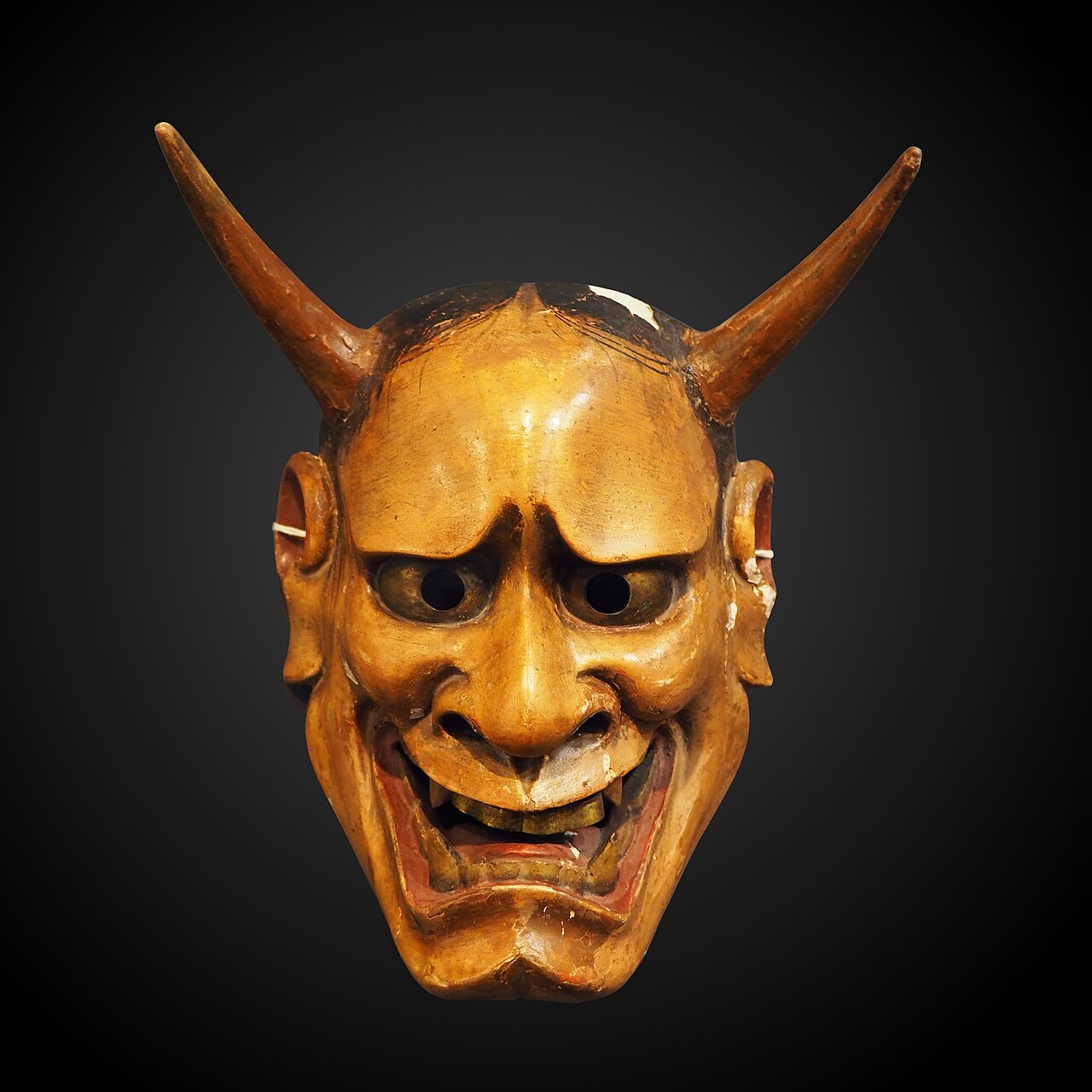 Carved wooden hannya mask with curved horns, bulging eyes and bared teeth against a dark background