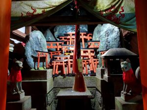 Two stone fox guardians in red bibs flanking a miniature torii altar at a Fushimi Inari sub-shrine