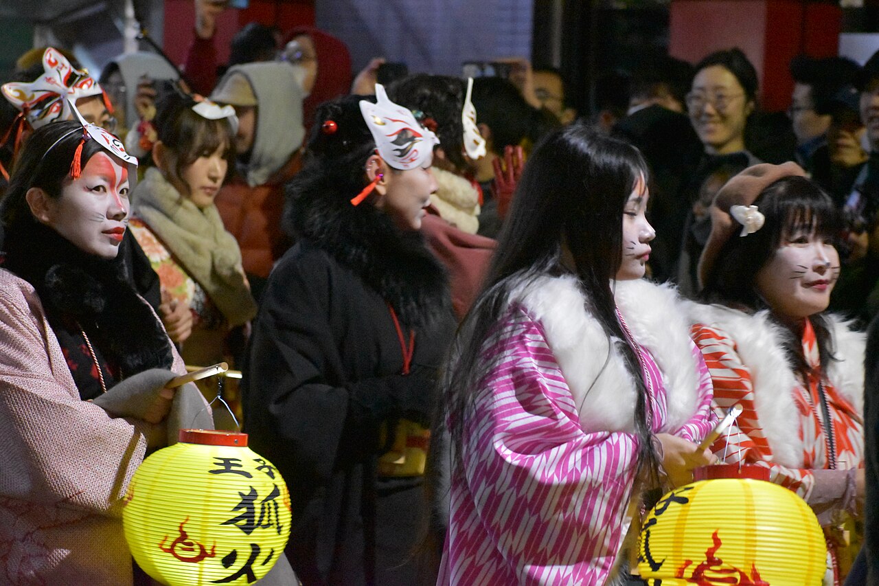Participants in kimono with kitsune masks and painted fox whiskers carrying lanterns at the Oji fox parade