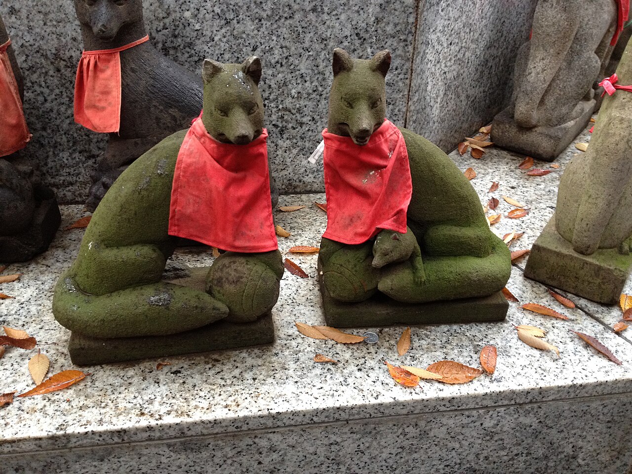 Moss covered stone fox statues in red bibs at an Inari shrine