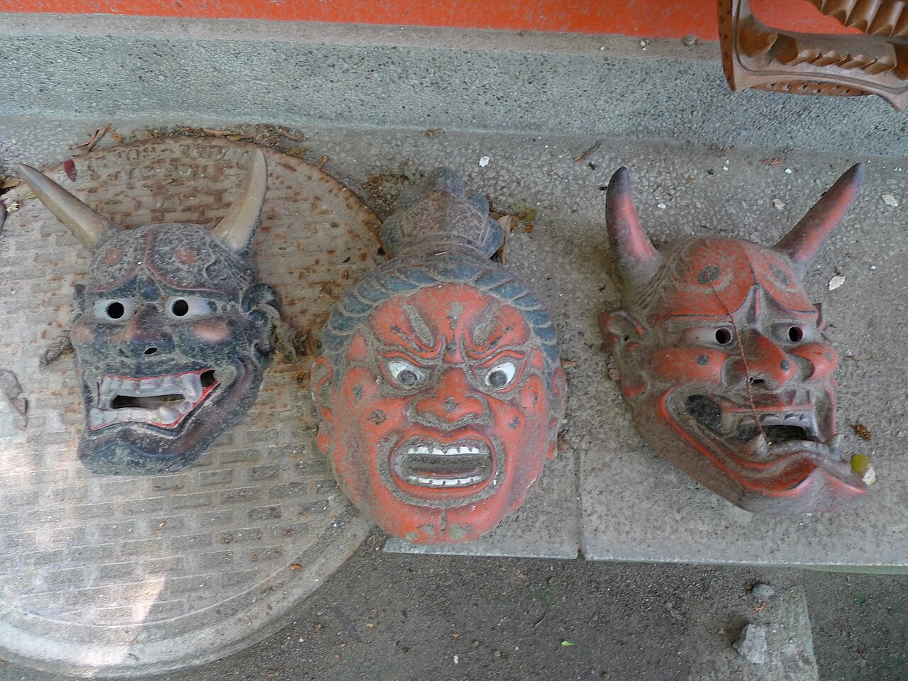 Three weathered hannya and oni masks with horns and fangs laid on stone paving at a Japanese shrine