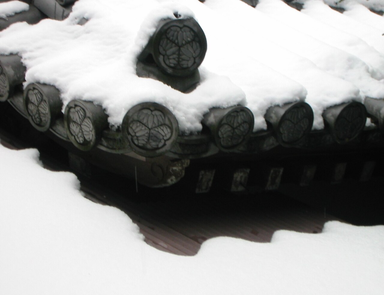 Snow-covered Japanese temple roof tiles each stamped with a circular three-leaf family crest