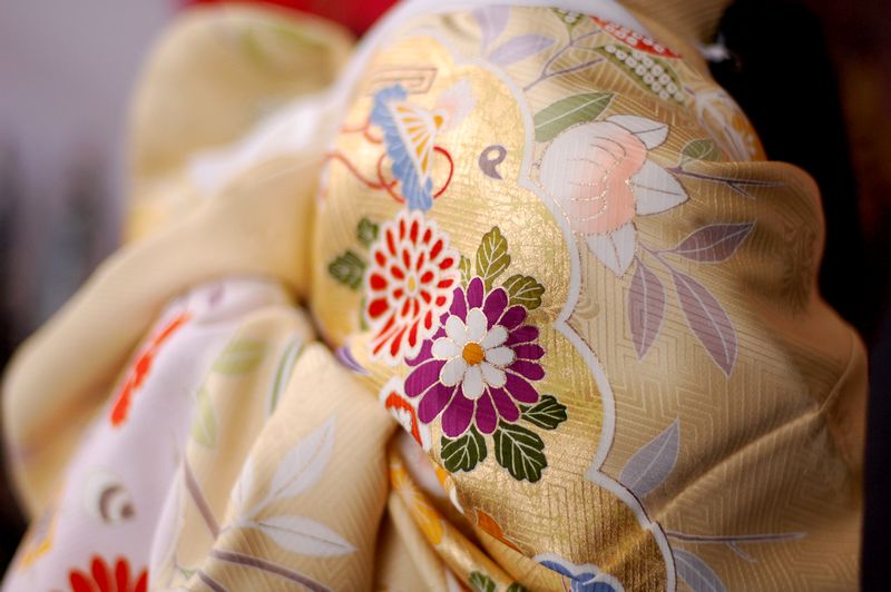 Close-up of gold kimono fabric printed with chrysanthemum and peony motifs in red, purple, and green