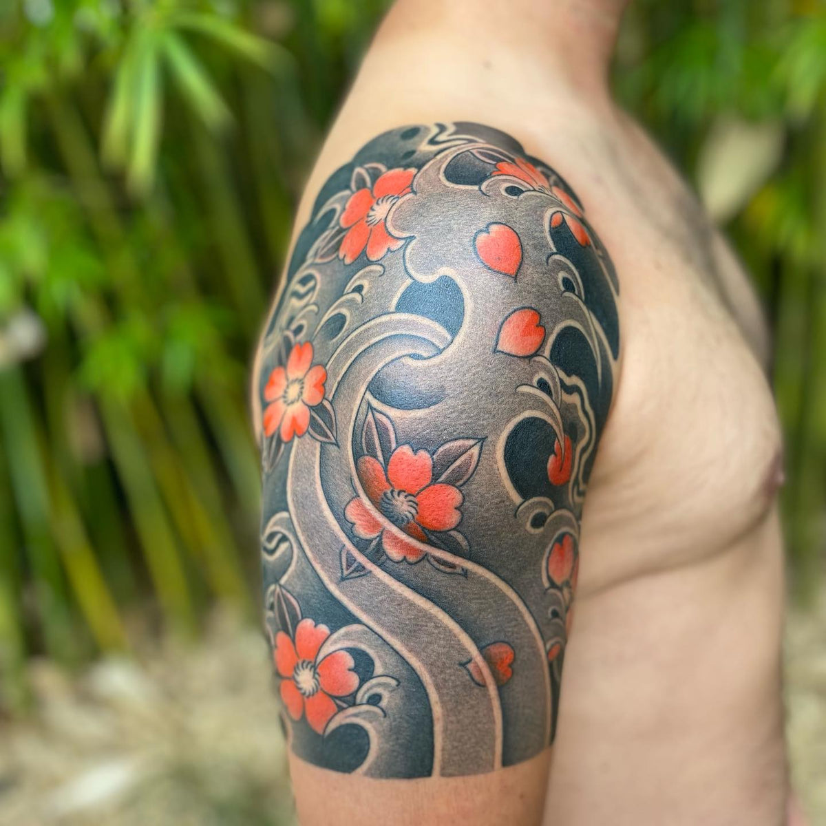 Japanese-style half-sleeve tattoo of red cherry blossoms set into grey wave and wind patterns on a shoulder