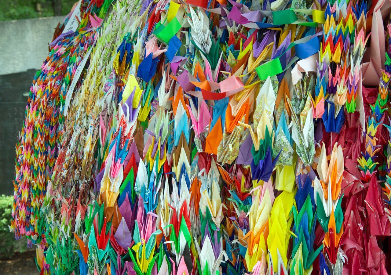 Thousands of brightly coloured folded paper cranes strung in dense curtains at a Hiroshima peace memorial
