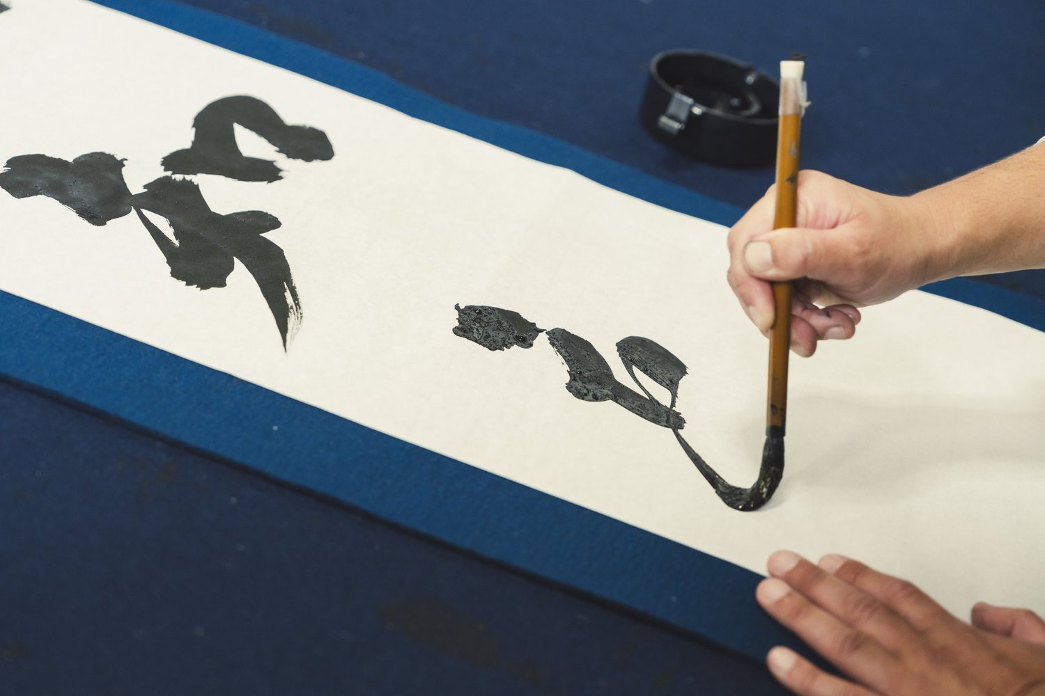 A calligrapher brushing kanji down a long sheet of paper in shodo practice