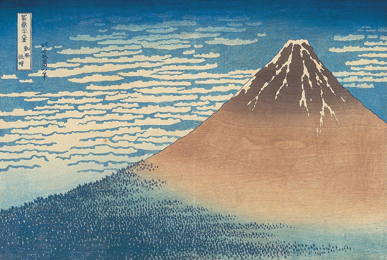 Hokusai print of Mount Fuji with a brown and rose slope, white snow streaks at the summit and banded clouds across a deep blue sky