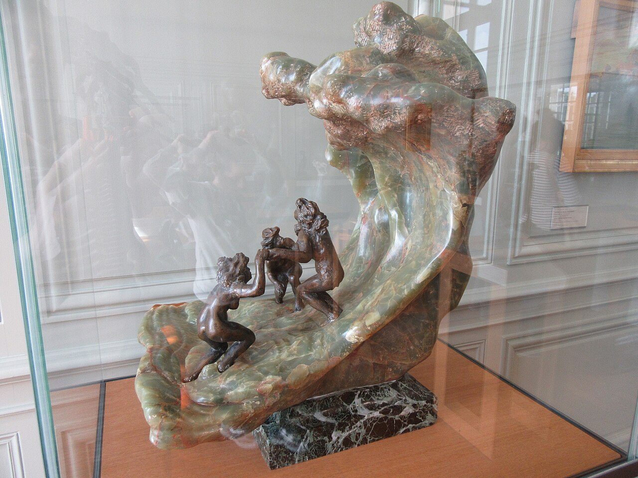Onyx sculpture of a curling green wave arching over three small bronze female figures crouched at its base