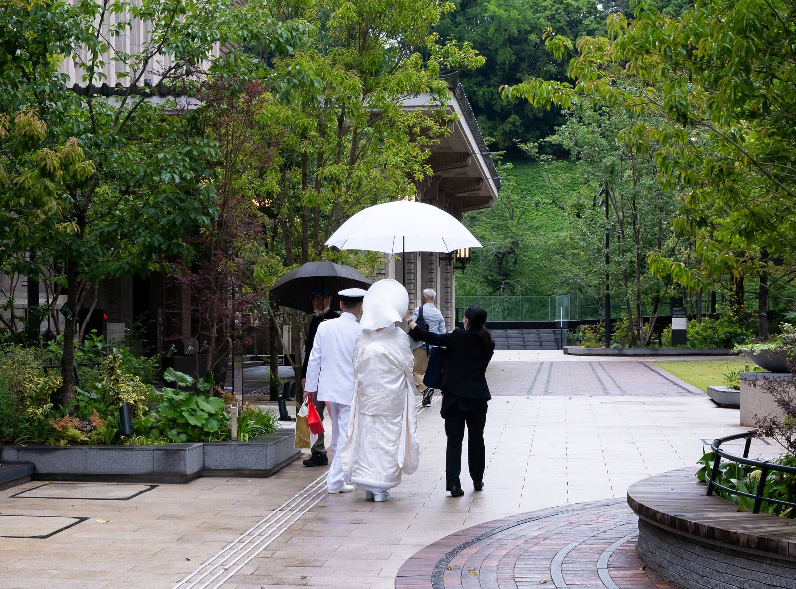 Japanese bride in an all-white shiromuku wedding kimono holding a pale wagasa parasol beside a wooden shrine building