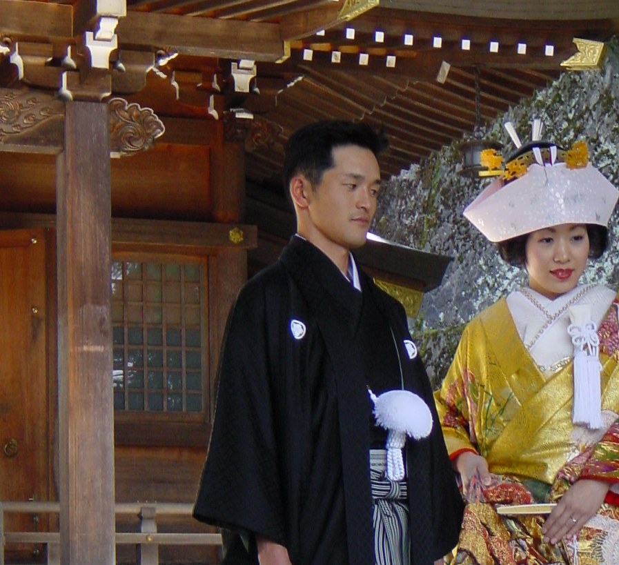 Groom in a black montsuki haori with white family crests on the sleeves, striped Sendaihira hakama and a kaku-obi sash