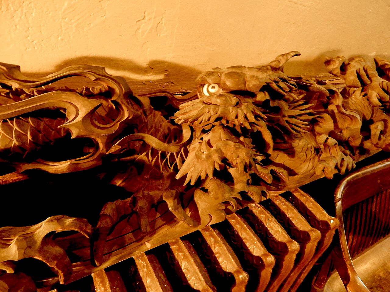 Carved wooden Japanese dragon head with horns and clawed foot on a temple beam