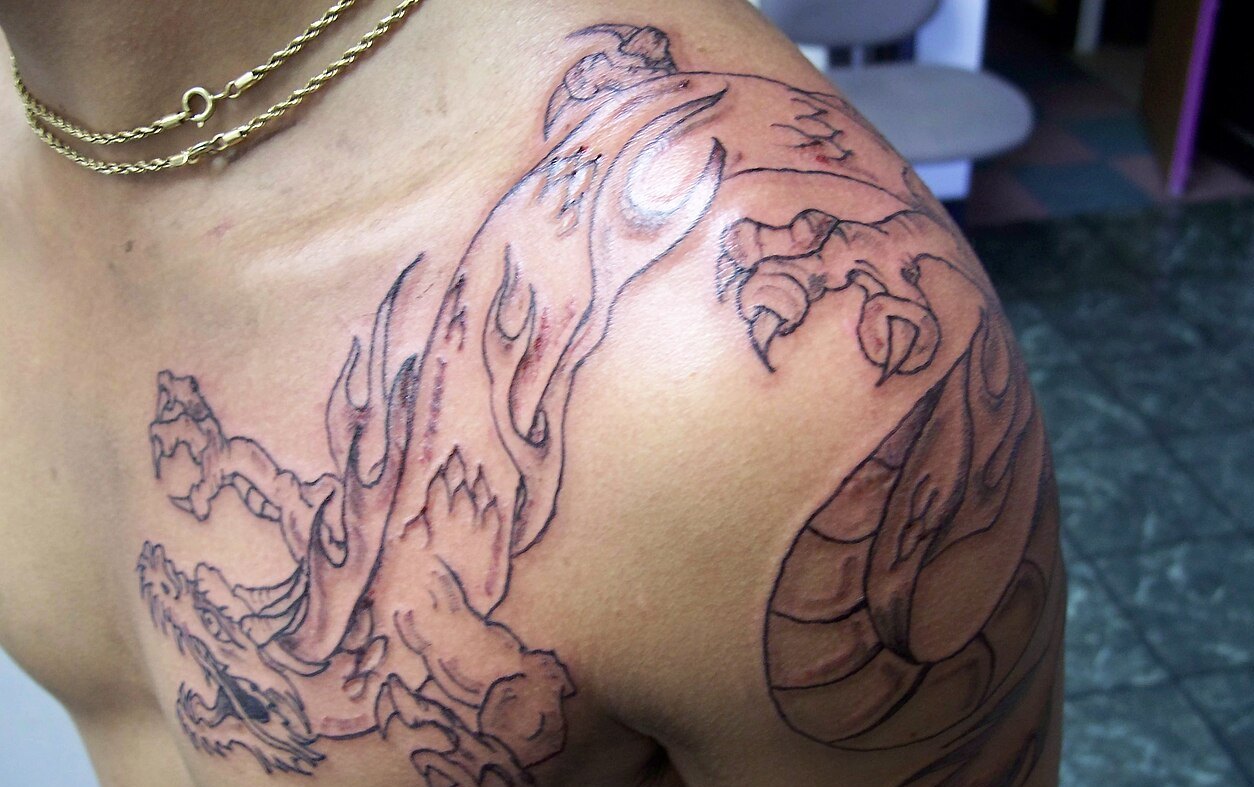 Line work of an Asian style dragon tattoo in progress across a chest and shoulder