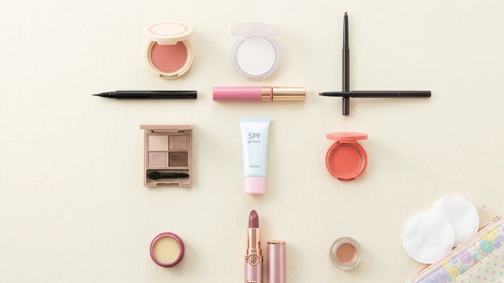 Flat lay of Japanese makeup products including blush compacts, translucent powder, brow pencil, liquid liner, an eyeshadow quad, SPF primer and lip gloss