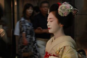 Maiko in a pale kimono wearing a silver and pink flower kanzashi in her hair