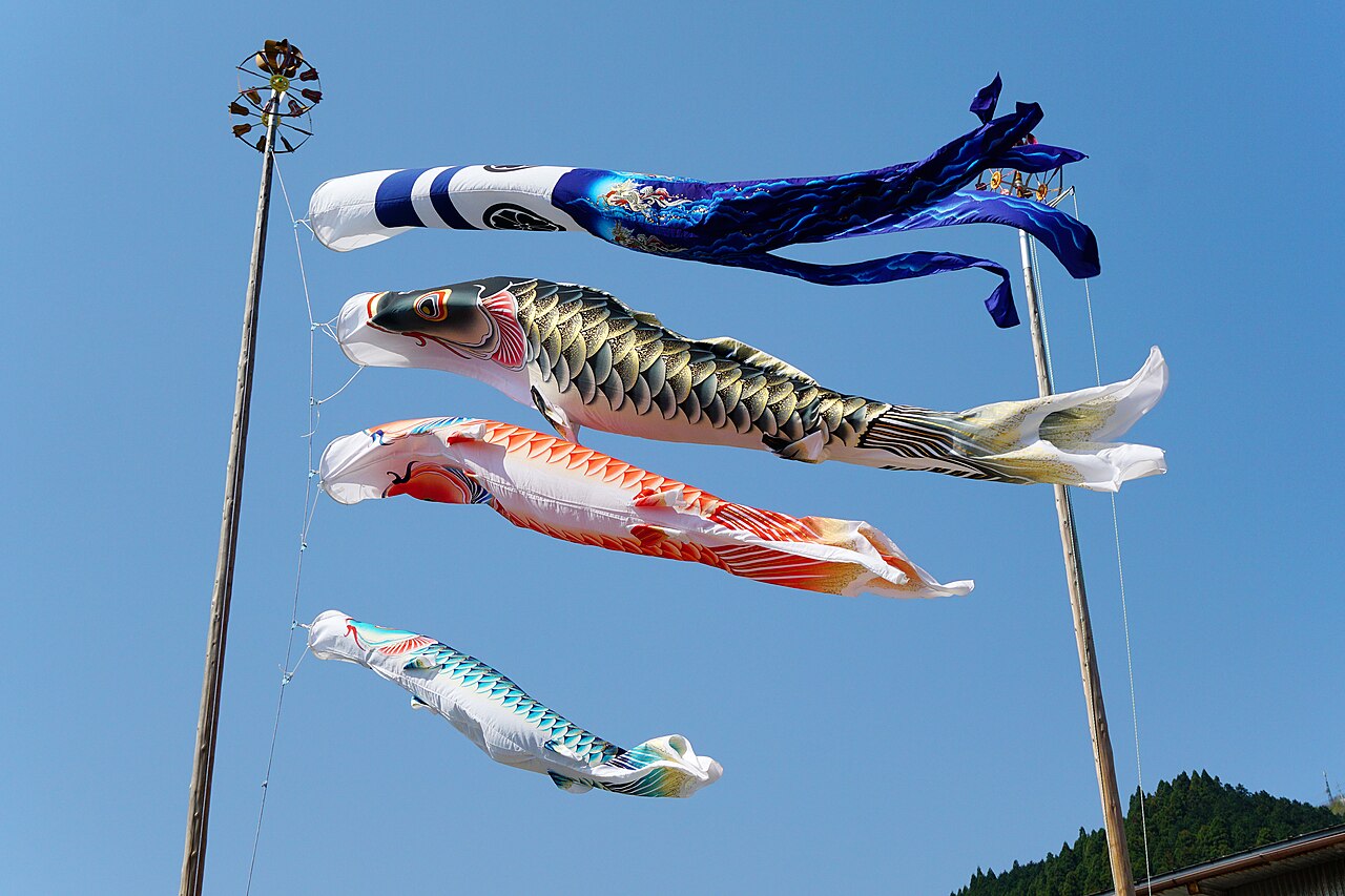 Black, red and blue carp-shaped windsocks flying on a pole against a blue sky