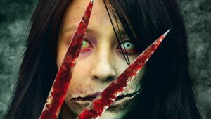 Pale long-haired woman with a mouth cut open at both corners, seen behind two blood-streaked blades