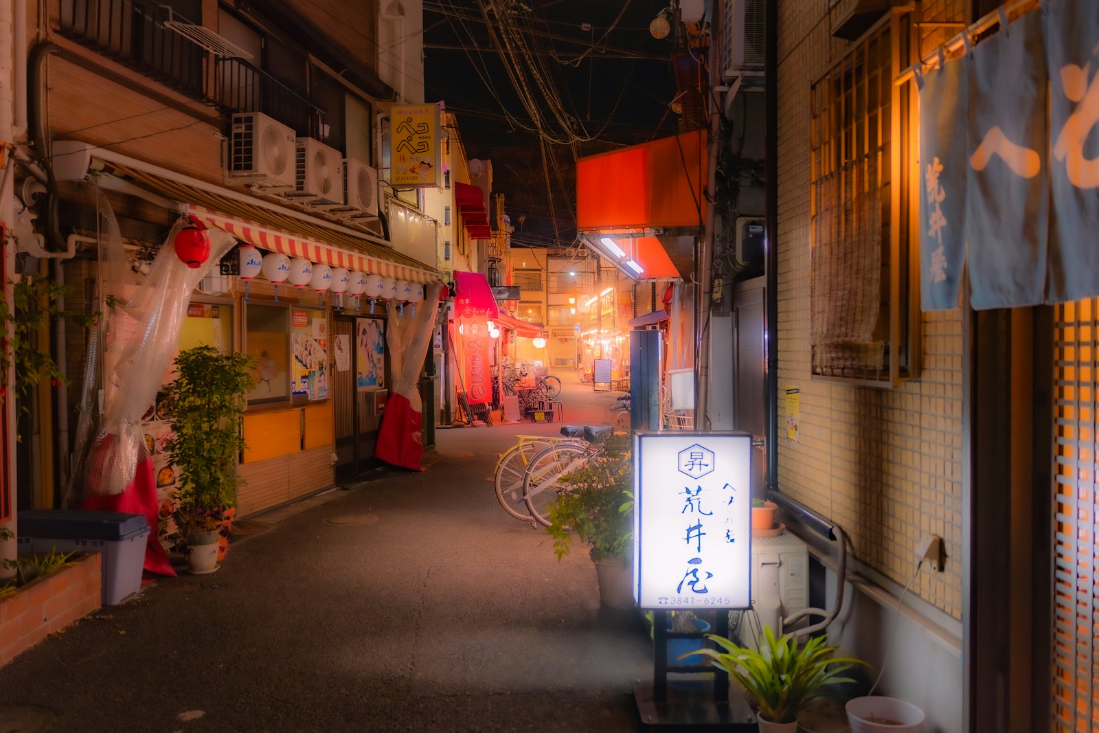 Empty Japanese shopping backstreet at night lit by red awnings, paper lanterns and a glowing shop sign