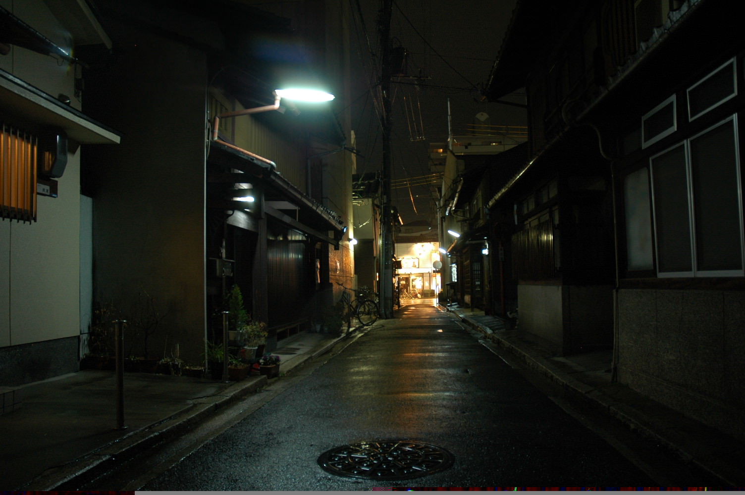 Deserted residential Japanese street at night lit by a single fluorescent street lamp with shuttered wooden houses