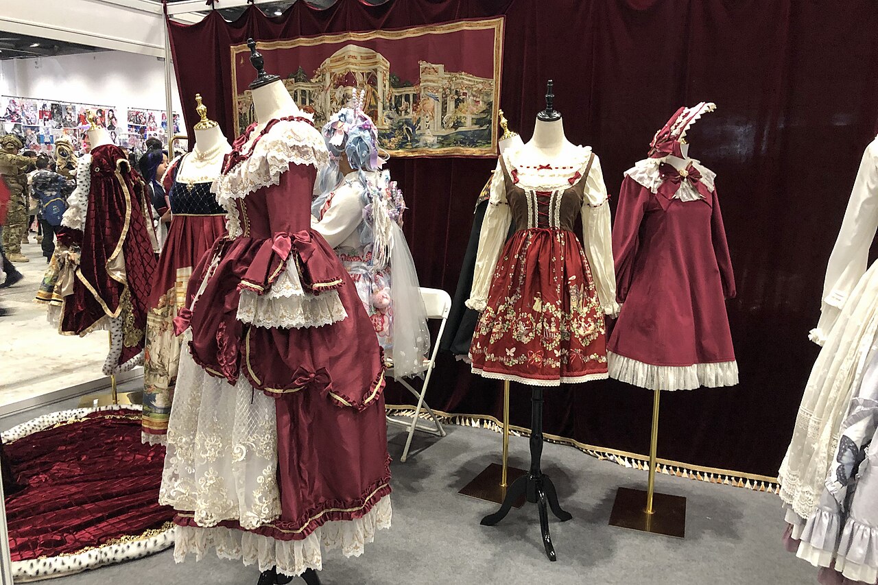 Burgundy and cream Classic Lolita dresses with lace trim and bows displayed on mannequins at a fashion convention booth