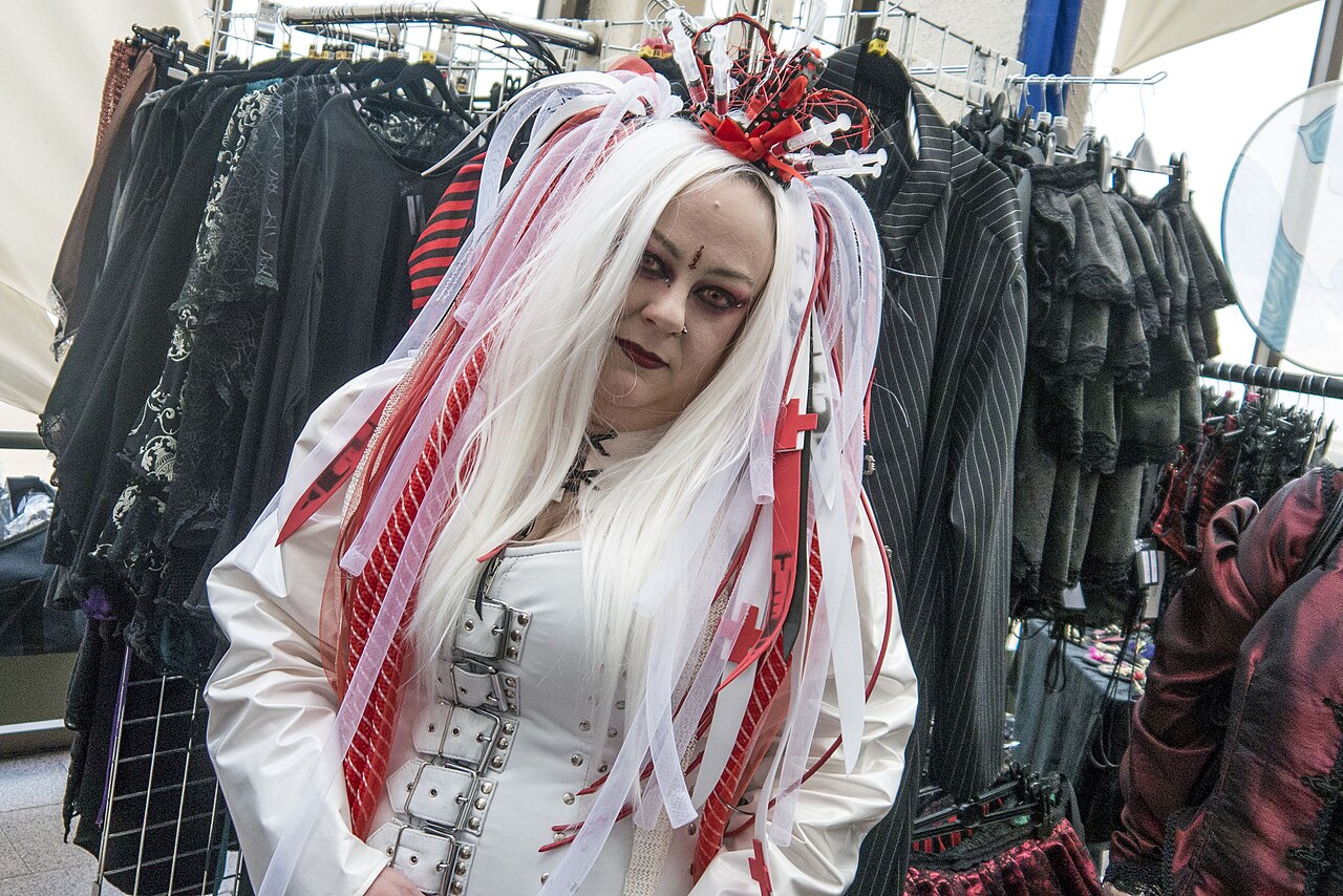 Attendee at a British goth festival with white hair, dark eye makeup and a white corseted outfit standing in front of racks of black clothing