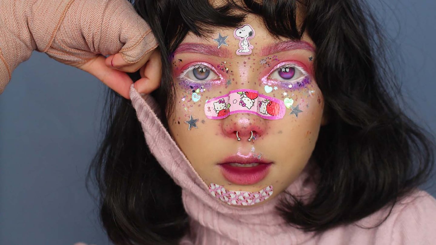 Close up of pastel pink menhera makeup with glitter, sticker bandages across the nose and a bandaged hand
