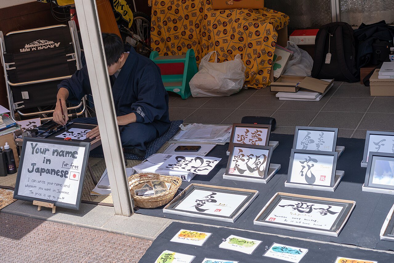 Calligrapher in a navy samue writing kanji with a brush at a street stall
