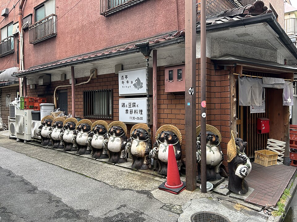 A row of ceramic Shigaraki tanuki statues wearing straw hats outside a restaurant in Tokyo