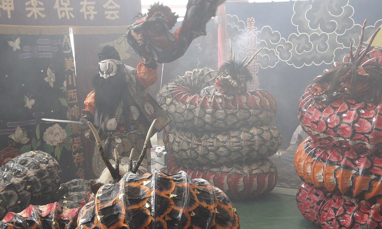 Iwami kagura performer as Susanoo above coiled serpent costumes in stage smoke