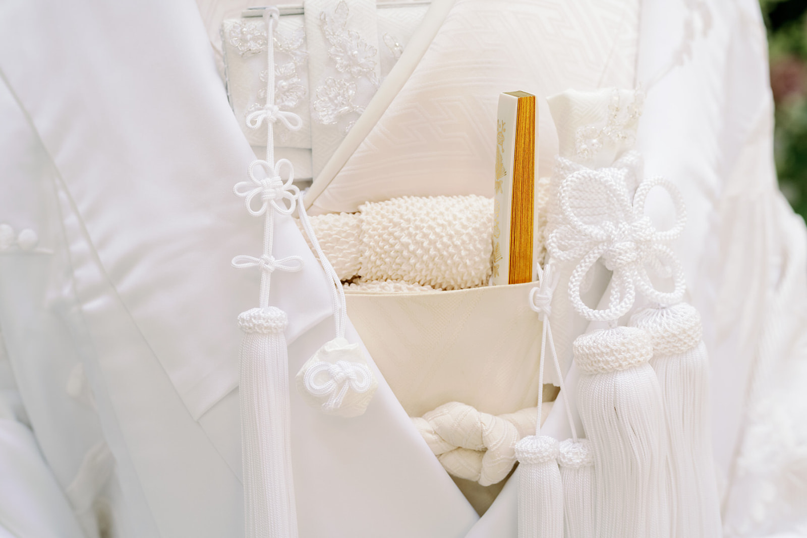 Close detail of a white shiromuku bridal kimono with hakoseko pouch, folding fan and tasselled cords