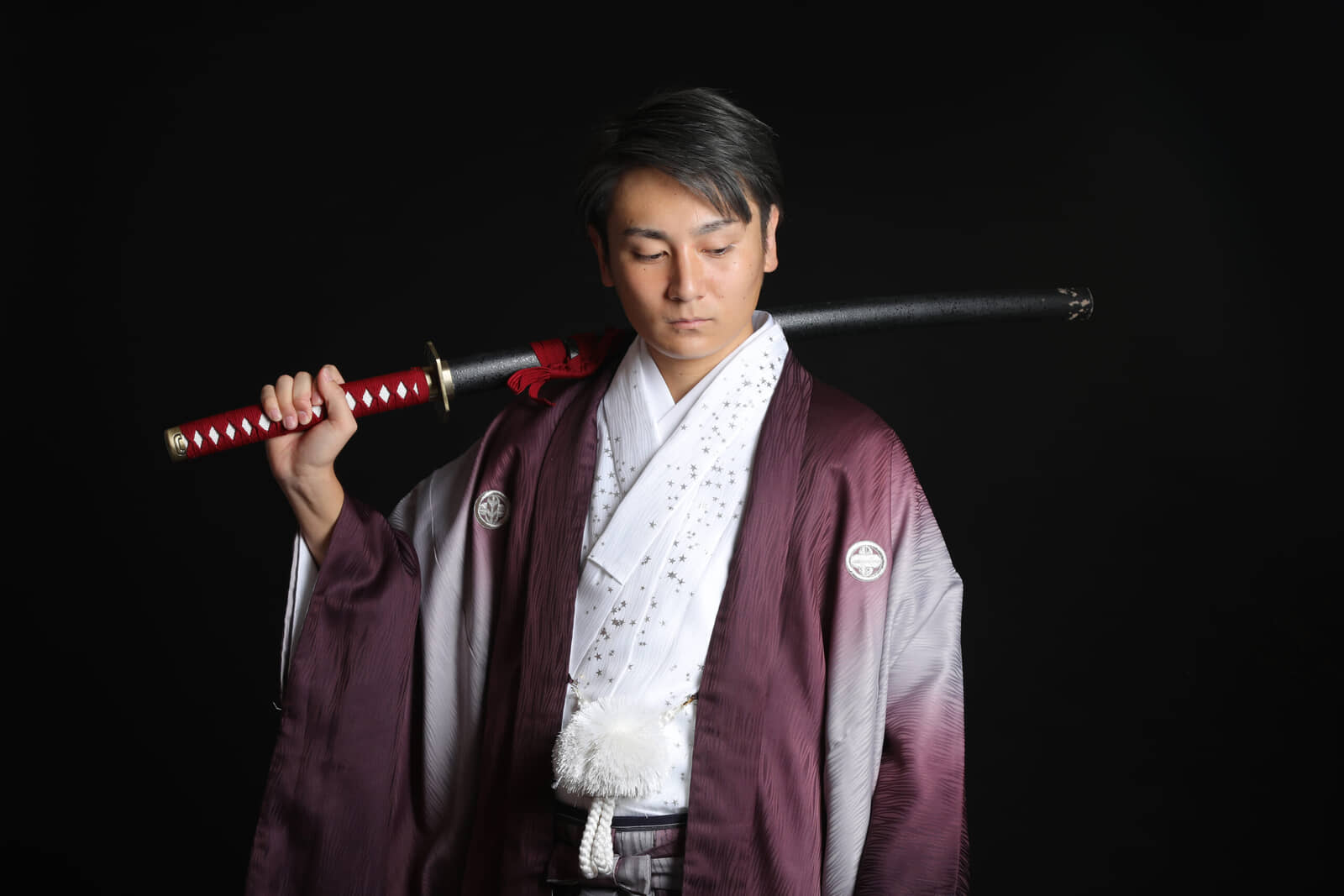 Man in a purple montsuki haori with white family crests holding a sheathed sword