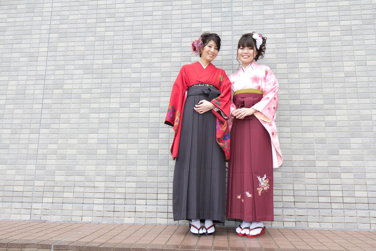 Two women in kimono with pleated hakama skirts and zori sandals at a graduation