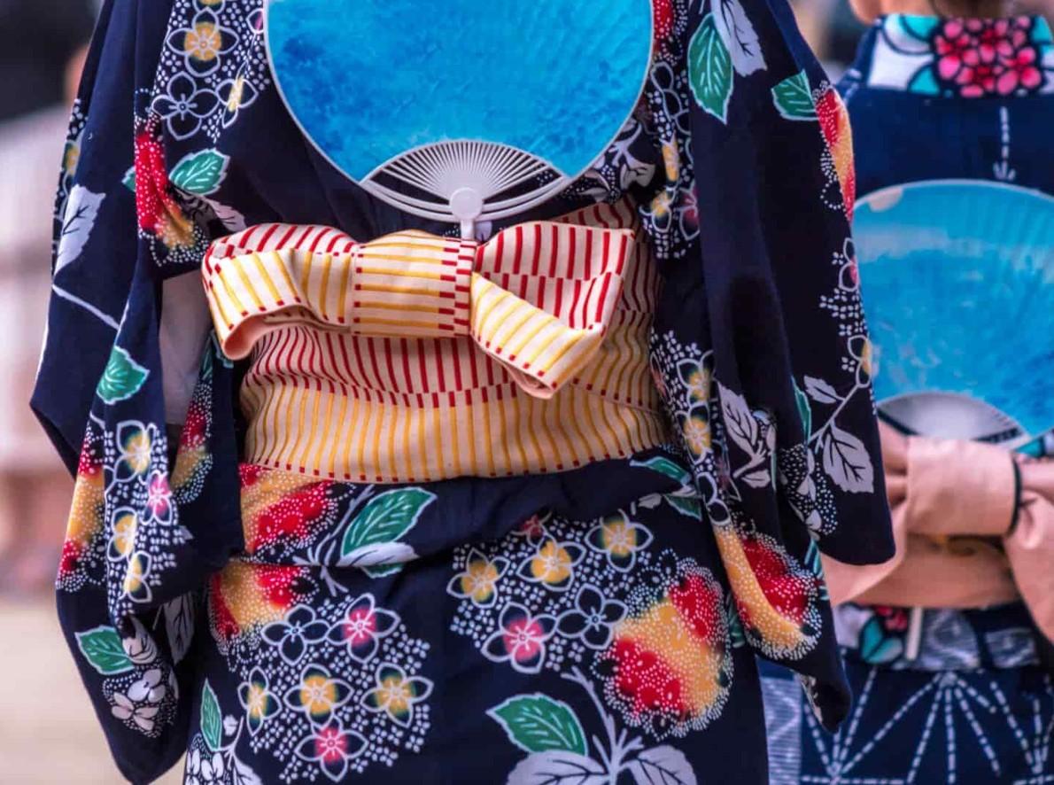 A yellow and red striped obi tied in a flat bow at the back of a navy yukata